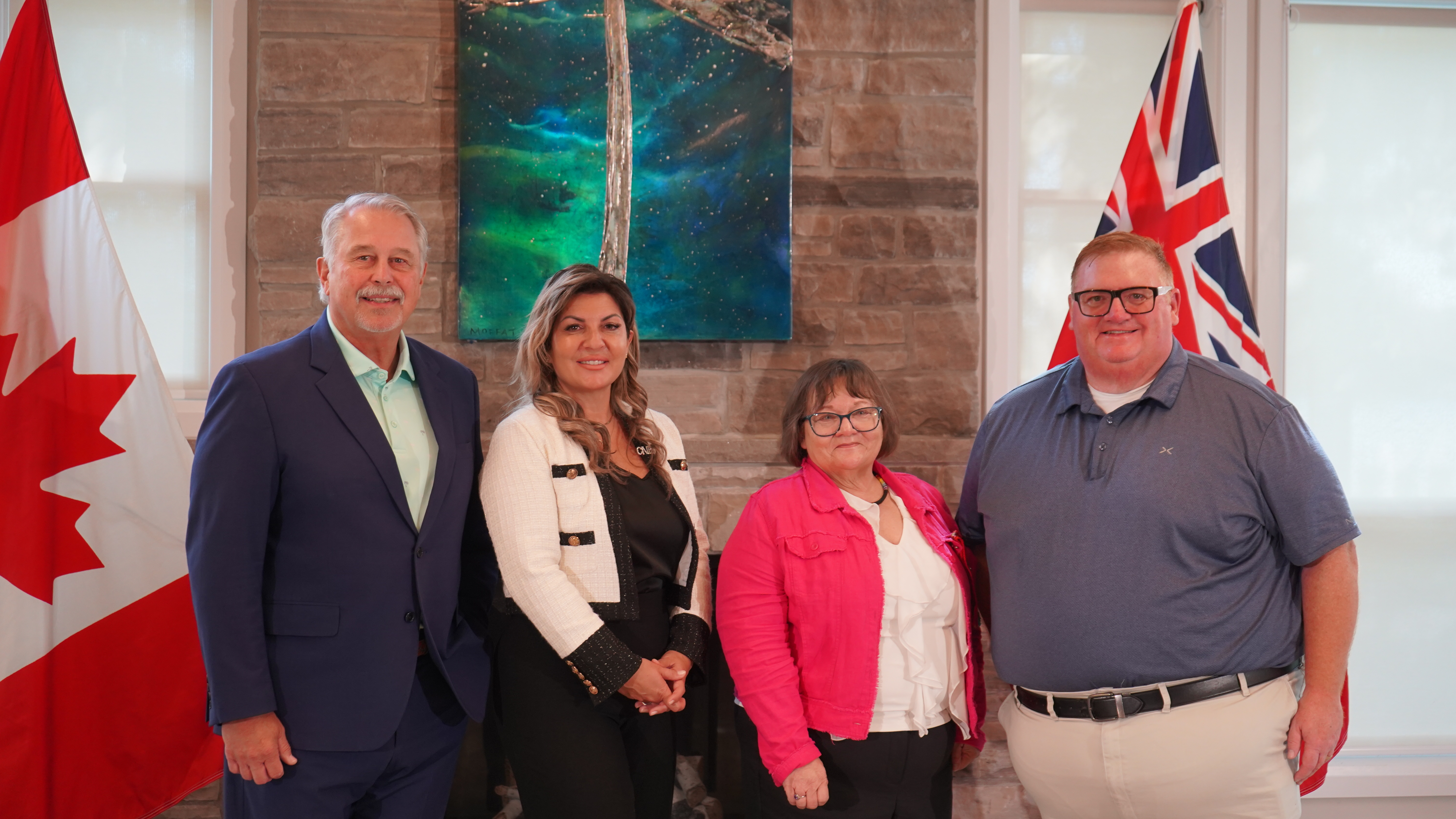L'honorable Neil Lumsden, ministre des Sports de l'Ontario, Angela Bonfanti, présidente-directrice générale de l'INCA, Sharon Cadeau, vice-présidente de la Nation métisse de l'Ontario, et l'honorable Graydon Smith, député provincial de Parry Sound–Muskoka, se tiennent devant la cheminée du centre Lake Joe de l'INCA. Les drapeaux du Canada et de l'Ontario sont à nos côtés.