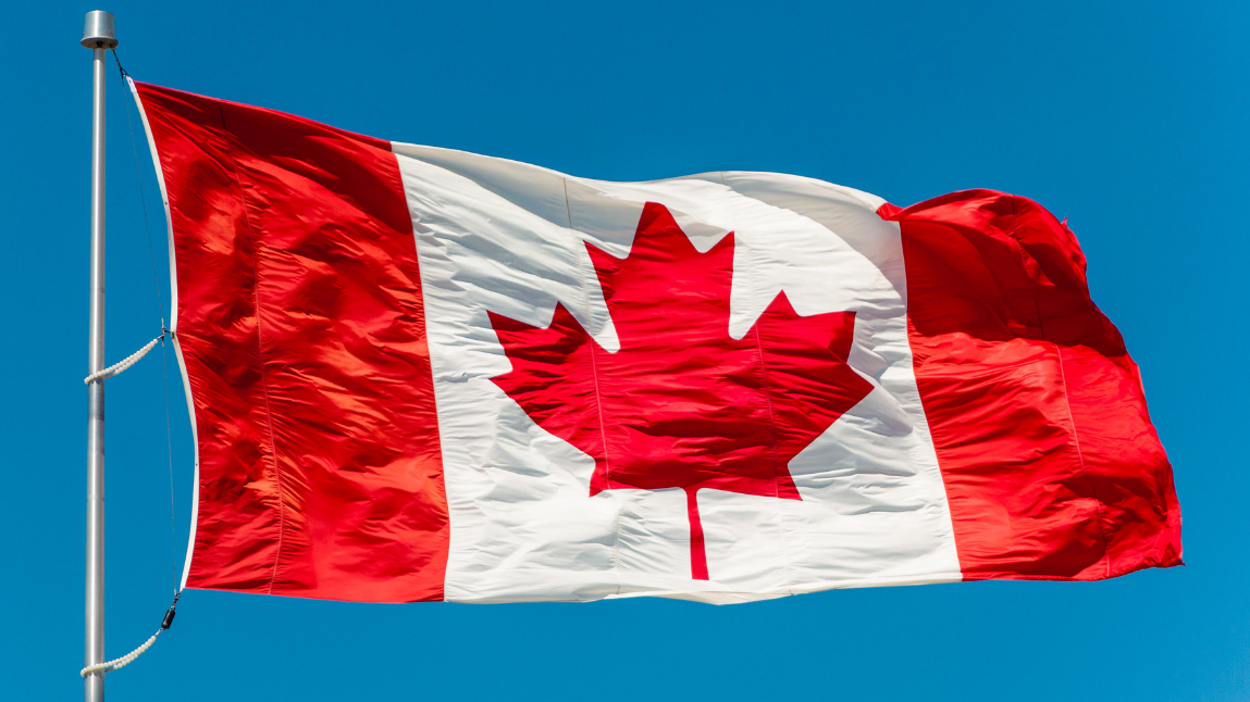 Un drapeau canadien flotte au sommet d'un mât, sur fond de ciel d'un bleu éclatant.