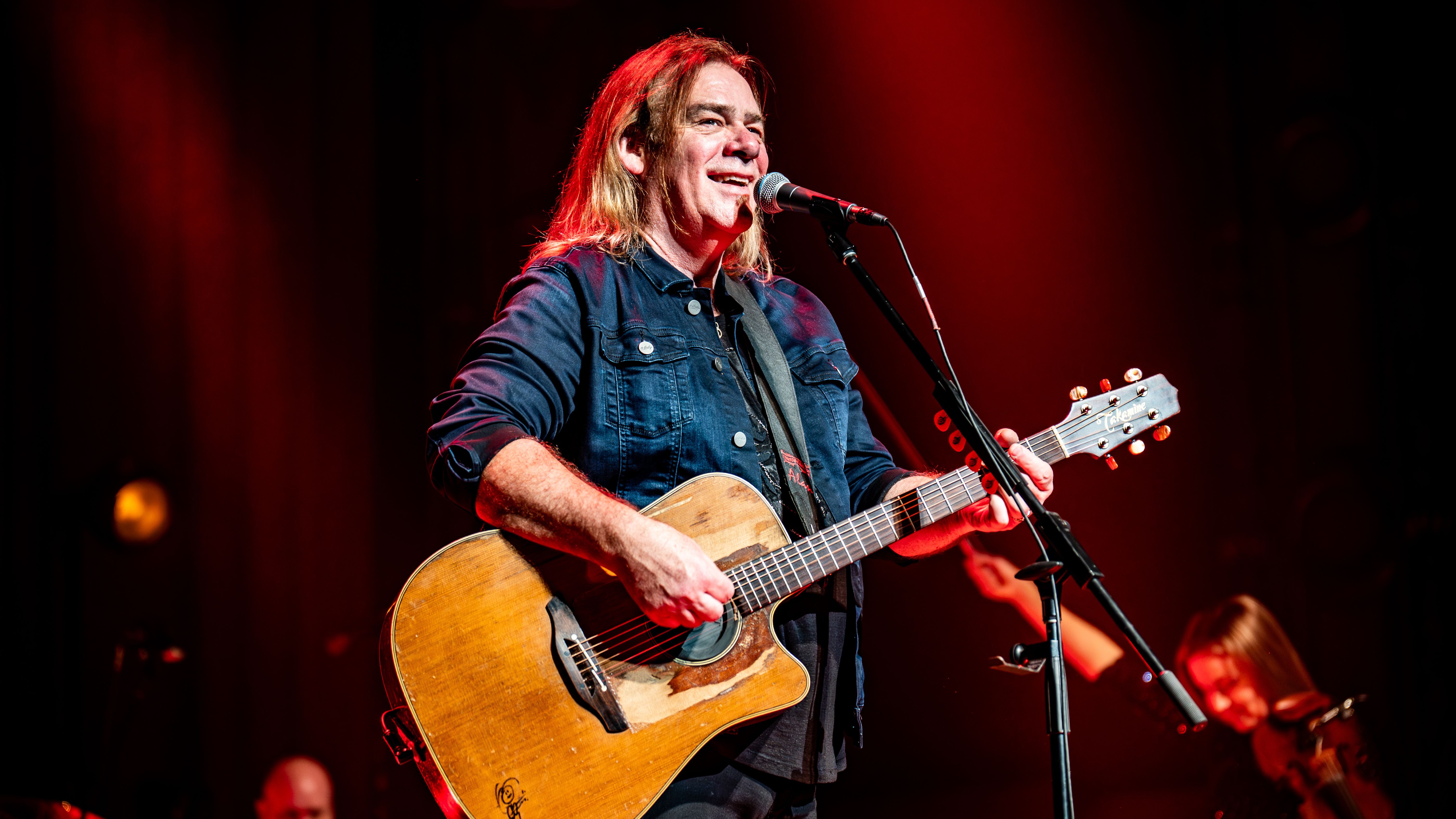 Le musicien Alan Doyle se tient sur scène devant un micro, une guitare à la main