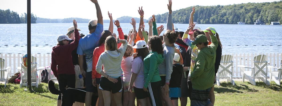 A group of young campers huddle in a circle. Arms are raised in the air.