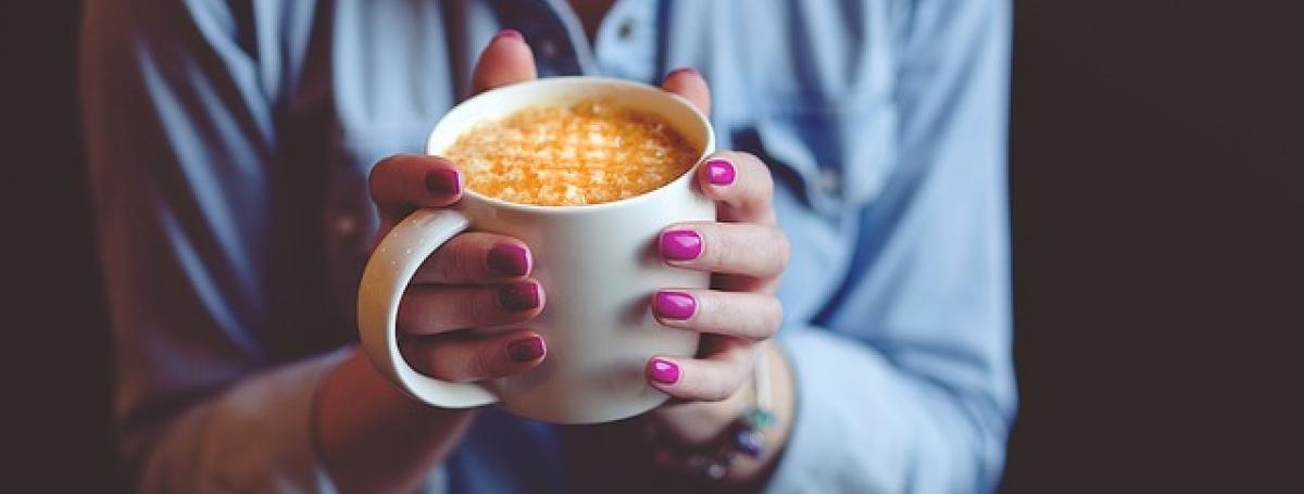 Des mains manucurées tiennent une tasse de café.