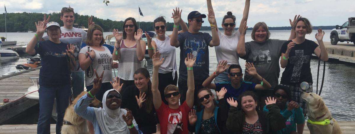 Participants posant en groupe sur un quai et saluant la caméra (prise en 2018).