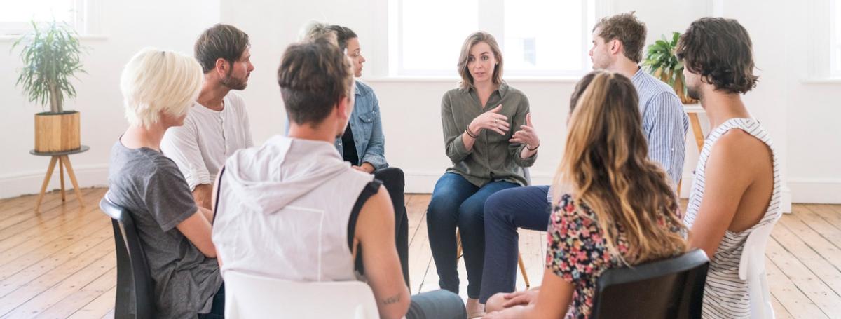 A group of 10 people sit in a circle and engage in lively conversation. 