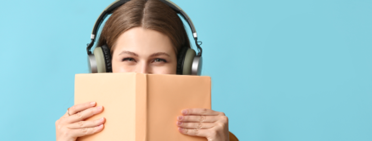 Une femme portant un casque d'écoute tient un livre devant son visage.