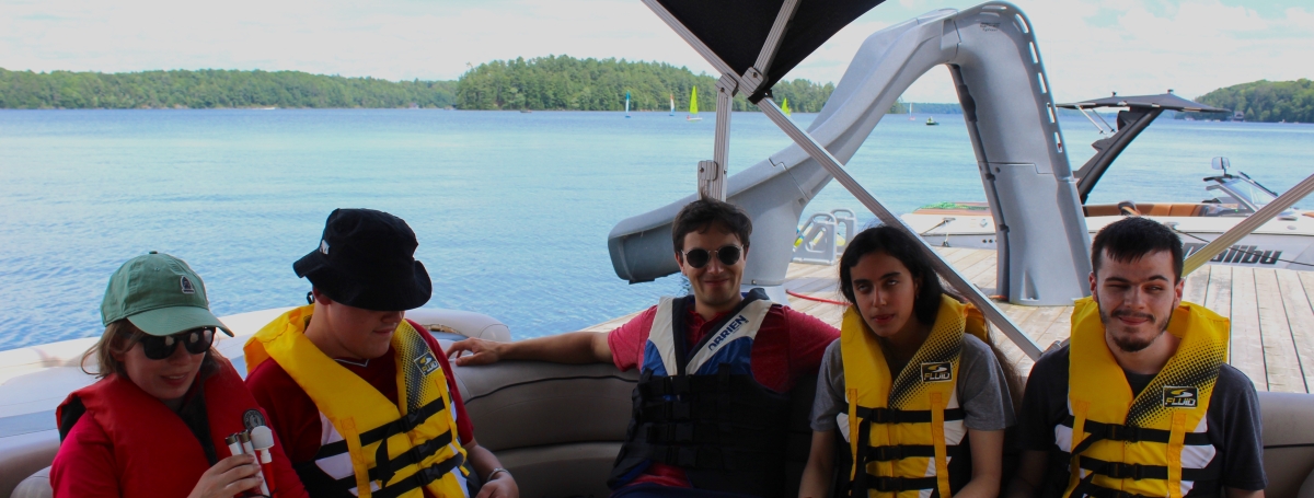 5 jeunes adultes portant une veste de sauvetage sur un bateau.
