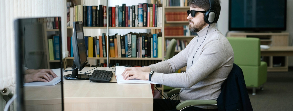Un homme aveugle avec des lunettes de soleil et un casque est en train de travailler sur son ordinateur.