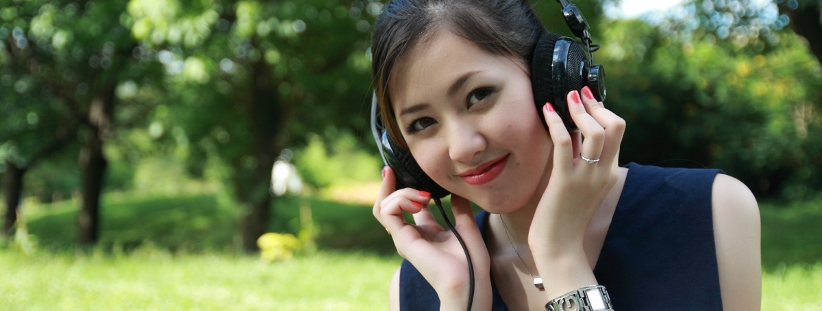 Une fille dans un parc porte un casque d'écoute et sourit.