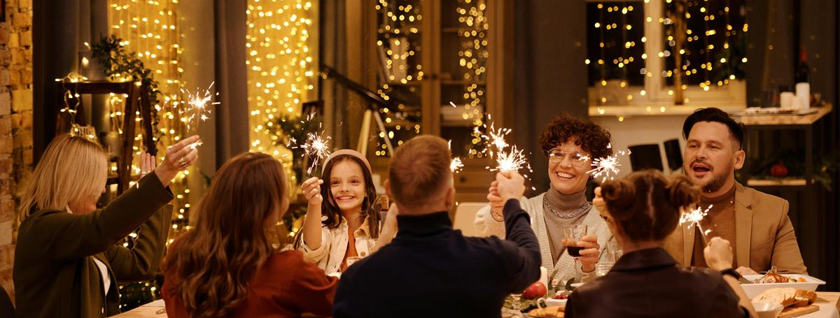 Une famille est à table et fête Noël. Pleins de guirlandes lumineuses sont accrochées aux fenêtres.