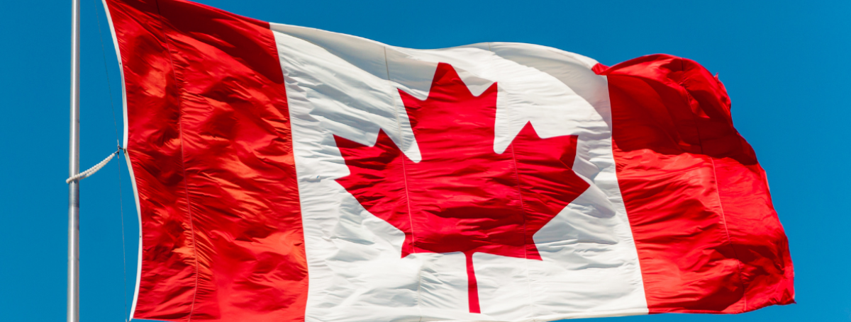 Un drapeau canadien flotte au sommet d'un mât, sur fond de ciel d'un bleu éclatant.