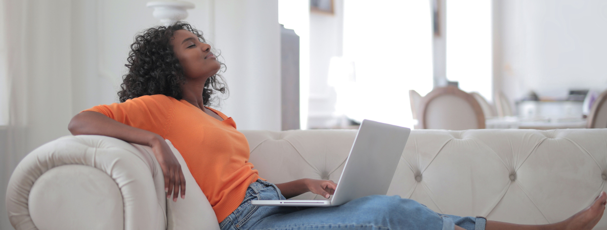 Une femme se détend sur son divan devant son ordinateur.