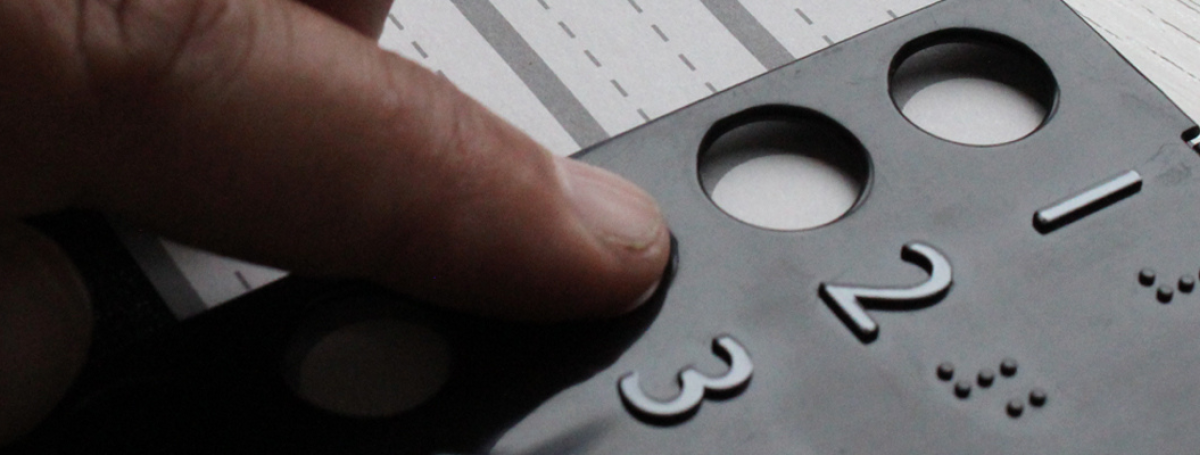 Gros plan sur une main qui explore au toucher un gabarit de vote tactile en relief, avec des chiffres 1, 2, 3 et leurs équivalents en braille, posé sur un bulletin de vote.