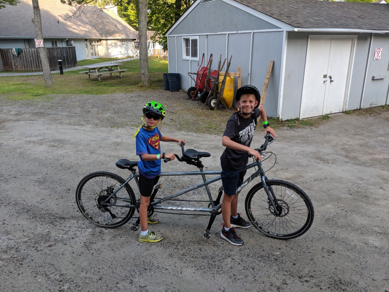 Deux campeurs sont assis à califourchon sur un vélo tandem sur un chemin de gravier.