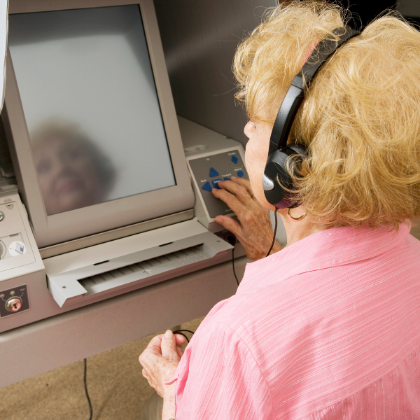 Une femme âgée, équipée d'écouteurs, utilise une machine à voter à écran tactile adaptée aux personnes à mobilité réduite, la main posée sur les commandes tactiles situées à côté de l'écran.