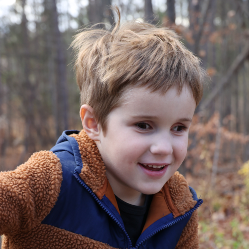 A young boy with sight loss smiles while outside on a fall day.