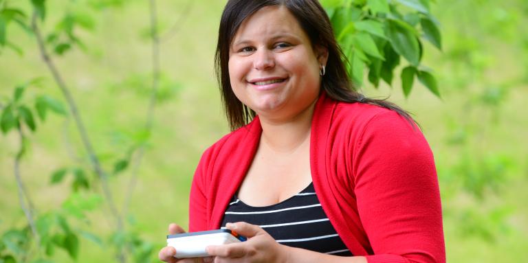 Woman with magnifier in her hand sitting among greenery.