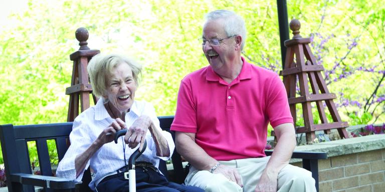 An older woman and man sitting on a bench laughing