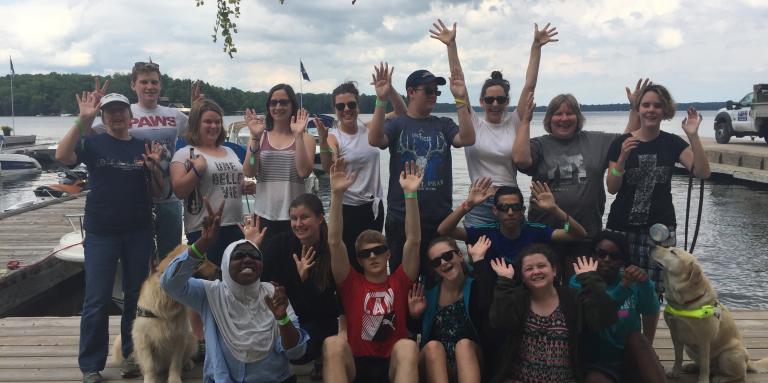 Participants posant en groupe sur un quai et saluant la caméra (prise en 2018).