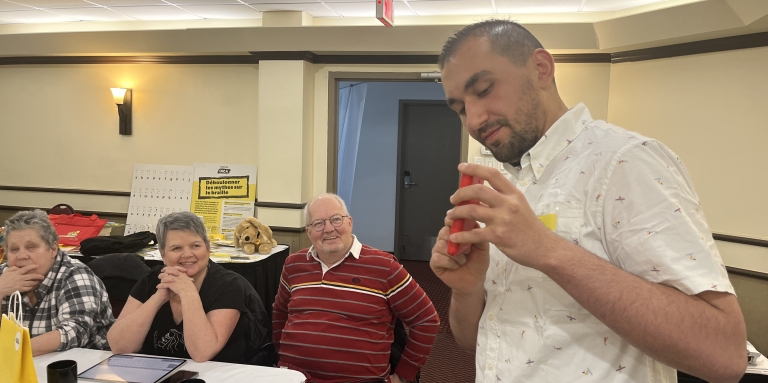 Mazen présente le téléphone Blindshell  devant des personnes souriantes et à attentives