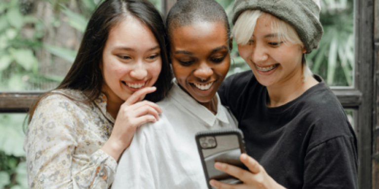 Trois jeunes femmes sur un téléphone cellulaire sourient.