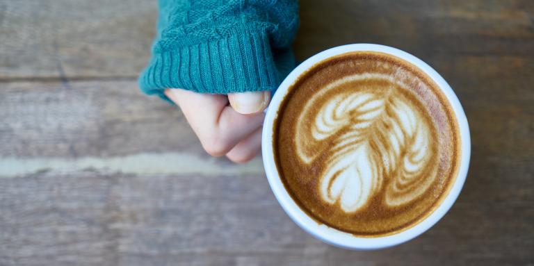 Une main tenant un café latté avec un dessin de coeur dans le lait.