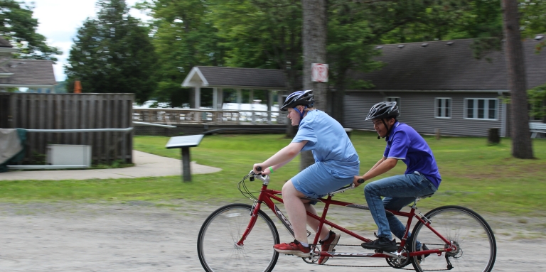 Two boys riding a red tandem bicycle