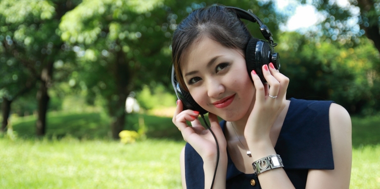 Une fille dans un parc porte un casque d'écoute et sourit.