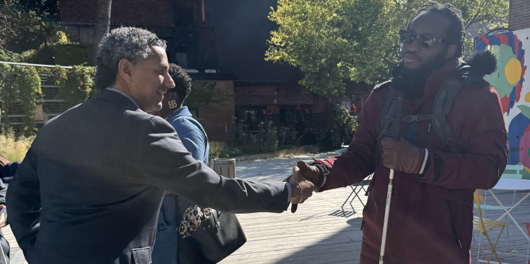 un candidat au municipal qui salue un homme en lunette noire et qui tient une canne blanche sur son autre main