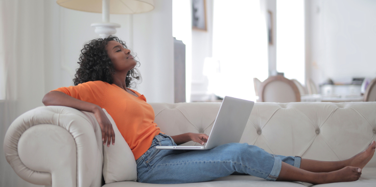 Une femme se détend sur son divan devant son ordinateur.