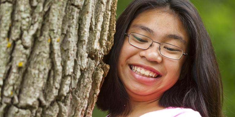 A close-up of a girl climbing up a tree, smiling at the camera