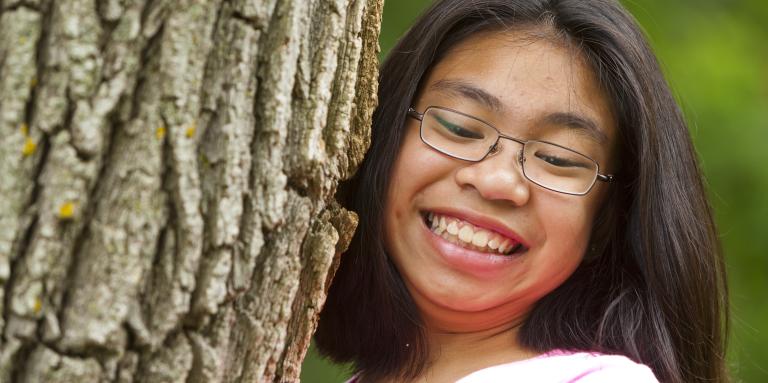 un gros plan d'une jeune fille qui grimpe à un arbre en souriant. Elle porte des lunettes.