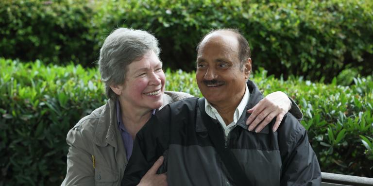 Un homme aveugle et une femme souriante assis sur un banc.