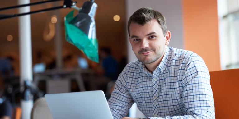 Un homme souriant tape sur un ordinateur portable.