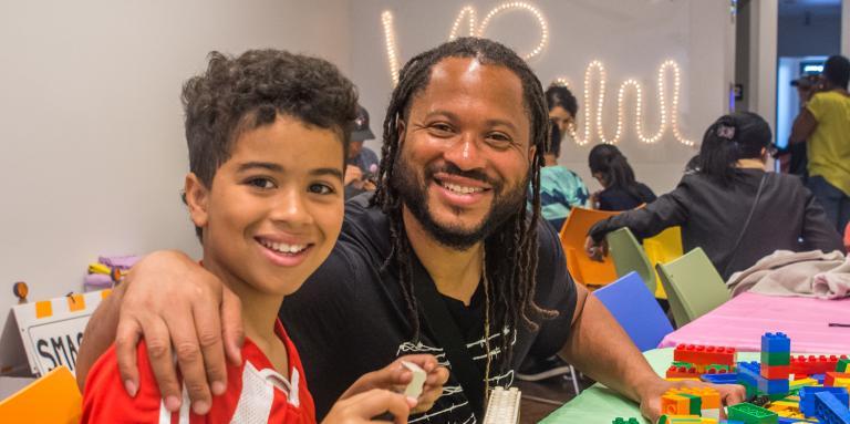 a father and son smiling and building lego. 