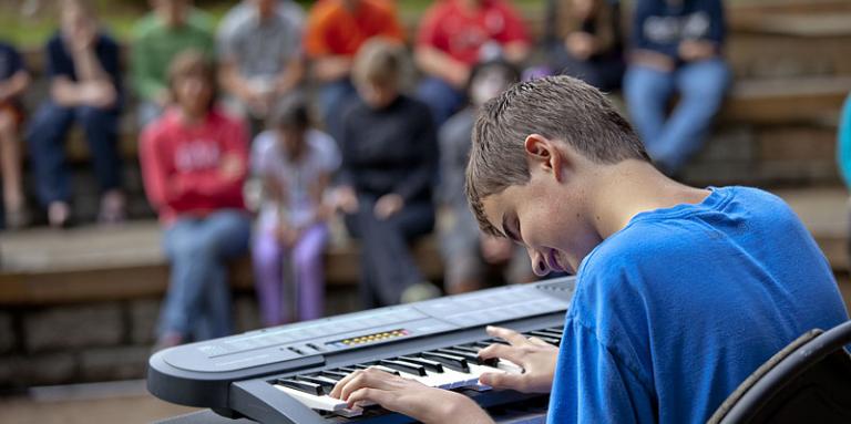 garçon ayant une perte de vision qui joue du clavier devant la foule