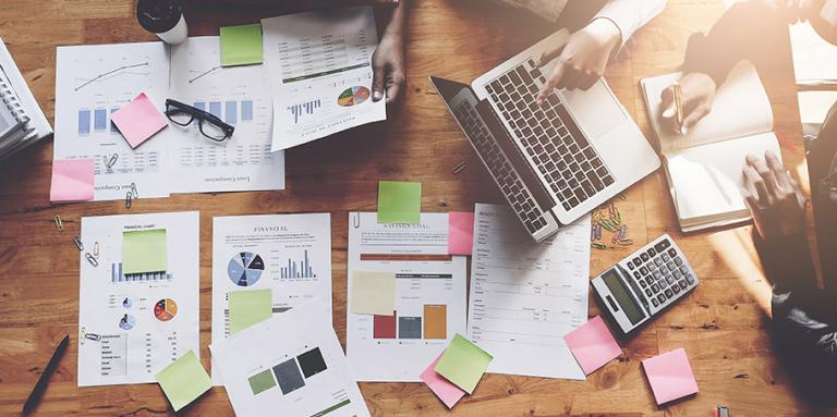 une vue en plongée de six personnes assises à une table travaillant sur des documents de recherche comprenant des graphiques et des tableaux.