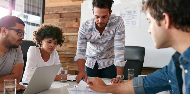 Trois hommes et une femme autour d’une table consultant des documents de recherche 