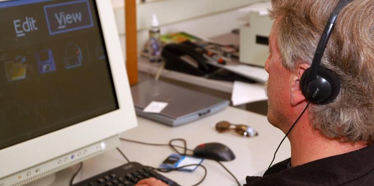 Un homme utilisant Zoomtext sur son ordinateur et ayant des écouteurs sur les oreilles