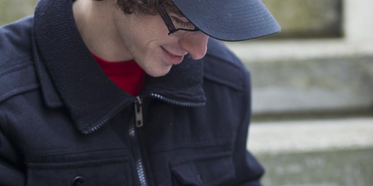 Man in black baseball cap looking through red magnifier