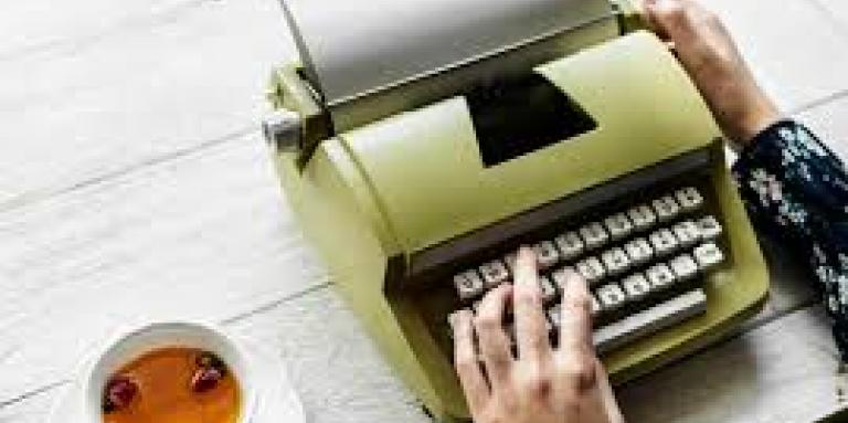 A person's hands type on a typewriter with a mug of tea beside them on the table.