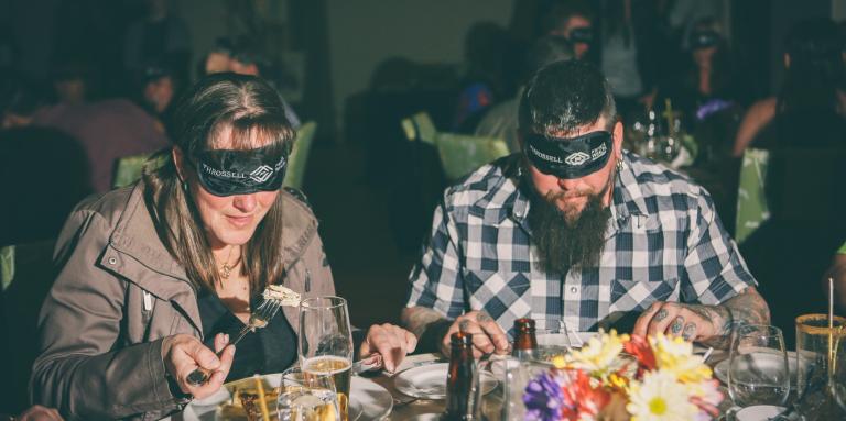 Deux convives dégustant un repas avec un bandeau sur les yeux.