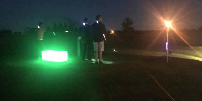 Golfers standing on the green with lights around themGolfeurs sur le vert entourés de lumières.