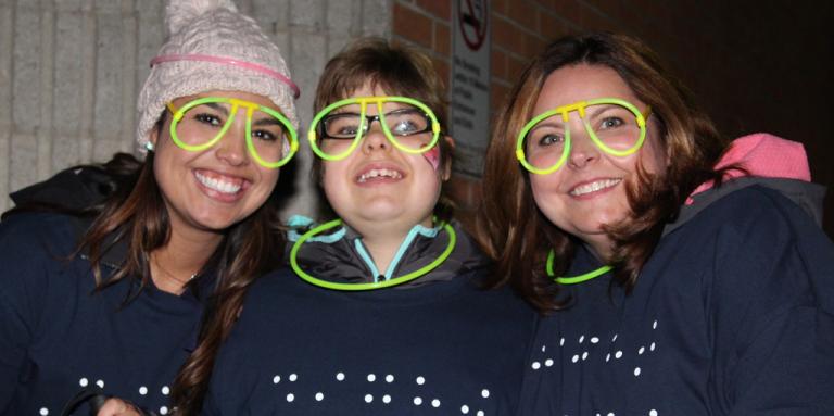Trois participants à Marchons le soir portant des lunettes lumineuses tout sourire.