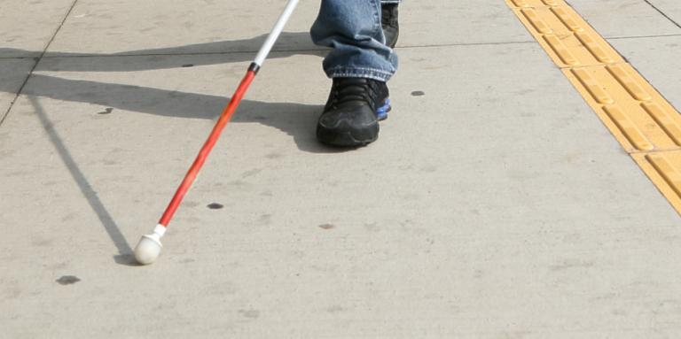 Pieds et canne blanche d'une personne marchant dans la rue