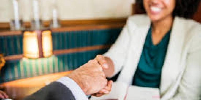 A woman smiles as she shakes a male colleague's hand across a table.