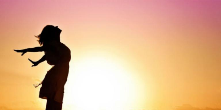 La silhouette d’une femme se tenant debout les bras tendus sur un coucher de soleil