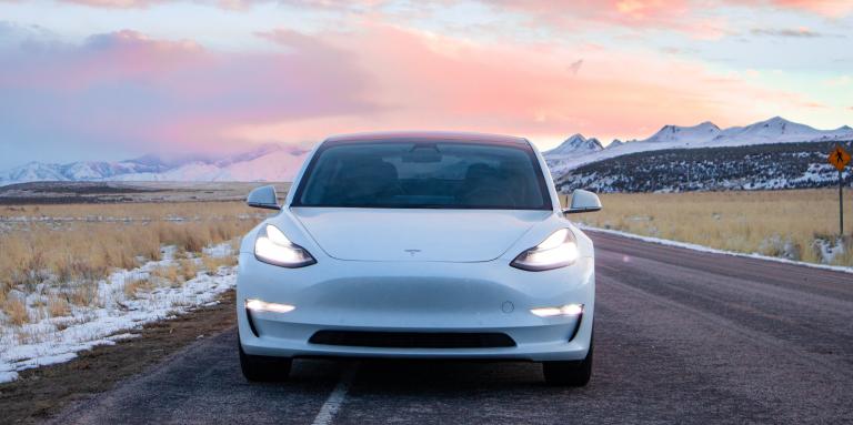 A white car drives along an asphalt road.