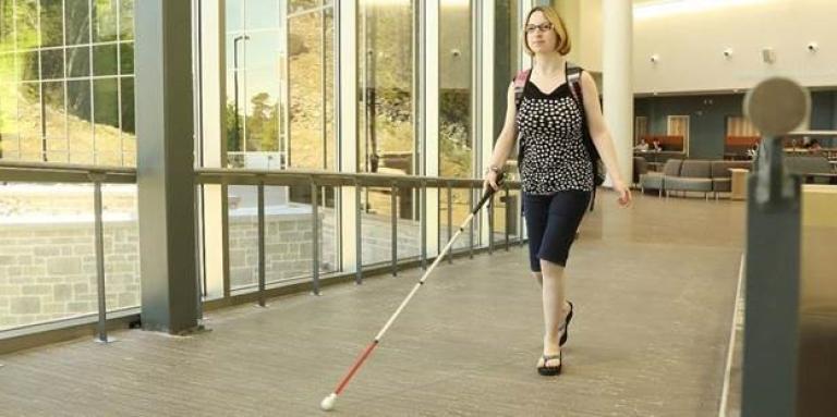 Femme marchant dans un couloir avec sa canne blanche