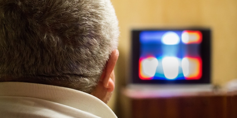 Homme aux cheveux gris regardant une télévision embrouillée.