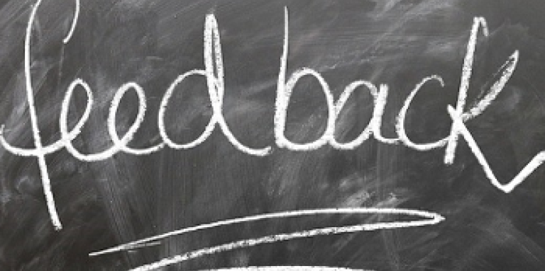 Un tableau noir sale sur lequel est écrit un texte en blanc à la craie. Texte « Feedback » (rétroaction).