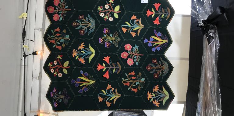 Courtepointe exposée dans un encan avec 18 alvéoles comprenant chacun des bouquets de fleurs colorés brodés.